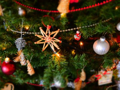 Joulukuuseen on ripustettu erilaisia joulukoristeita, kuten olkinen tähti, hopieinen pallo ja erilaisia värinauhoja
